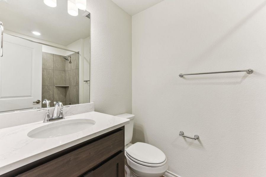 Bathroom featuring vanity, tiled shower, and a textured wall Bathroom featuring vanity, tiled shower, and a textured wall