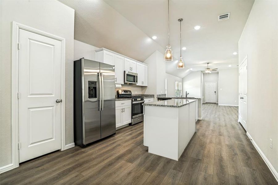 Modern kitchen featuring stainless steel appliances, white cabinetry, granite countertops, wood-finish flooring, and vaulted ceilings Modern kitchen featuring stainless steel appliances, white cabinetry, granite countertops, wood-finish flooring, and vaulted ceilings
