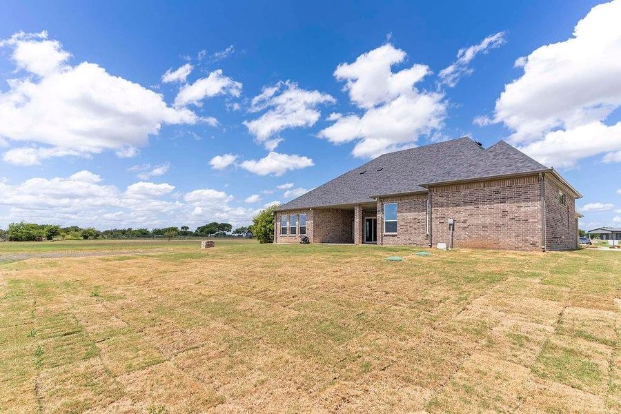 Back of property with a yard, brick siding, and a shingled roof