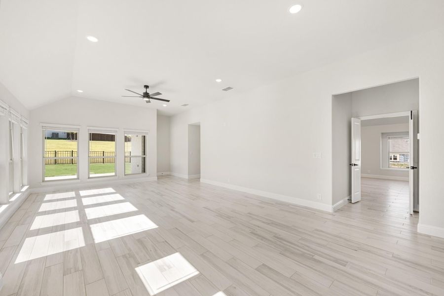 Open living room with vaulted ceiling, ceiling fan, light wood floors, and sliding glass doors to backyard