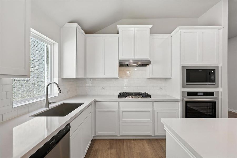 Kitchen with appliances with stainless steel finishes, tasteful backsplash, white cabinetry, and lofted ceiling Kitchen with appliances with stainless steel finishes, tasteful backsplash, white cabinetry, and lofted ceiling