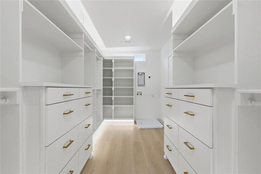 Spacious walk-in closet featuring custom white cabinetry with gold-finish hardware, extensive shelving, wood-finish flooring, and recessed ceiling lighting Spacious walk-in closet featuring custom white cabinetry with gold-finish hardware, extensive shelving, wood-finish flooring, and recessed ceiling lighting