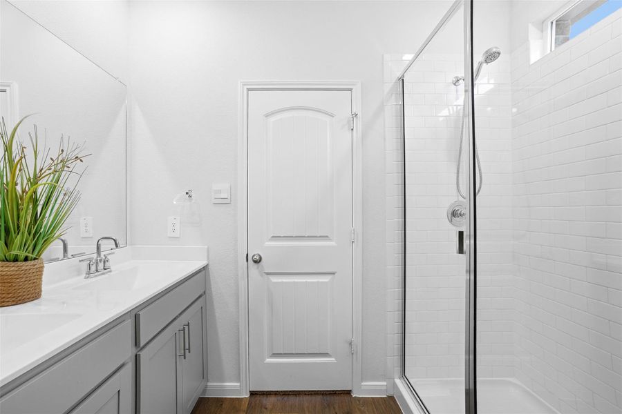 Bathroom with double vanity, a shower stall, and dark wood-style floors Bathroom with double vanity, a shower stall, and dark wood-style floors