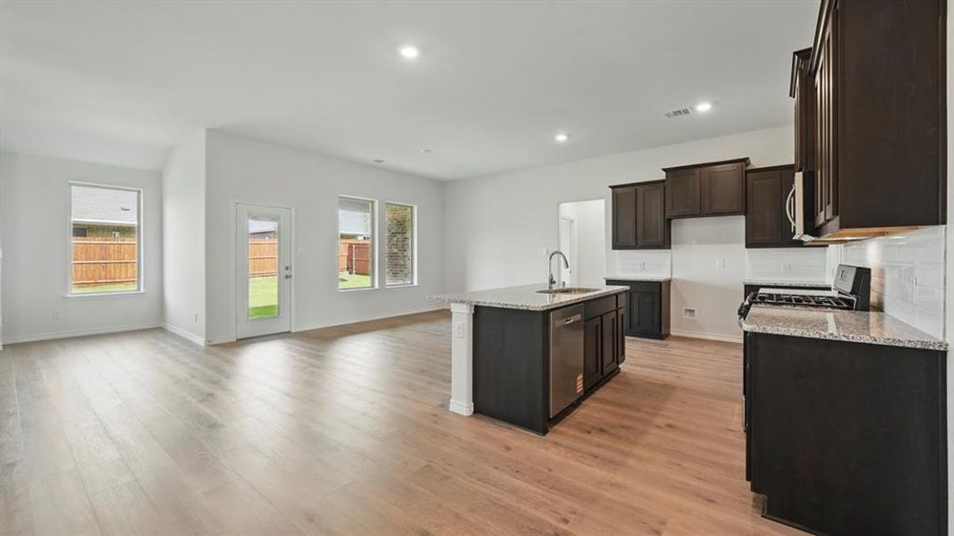 Kitchen featuring light stone countertops, tasteful backsplash, an island with sink, plenty of natural light, and recessed lighting