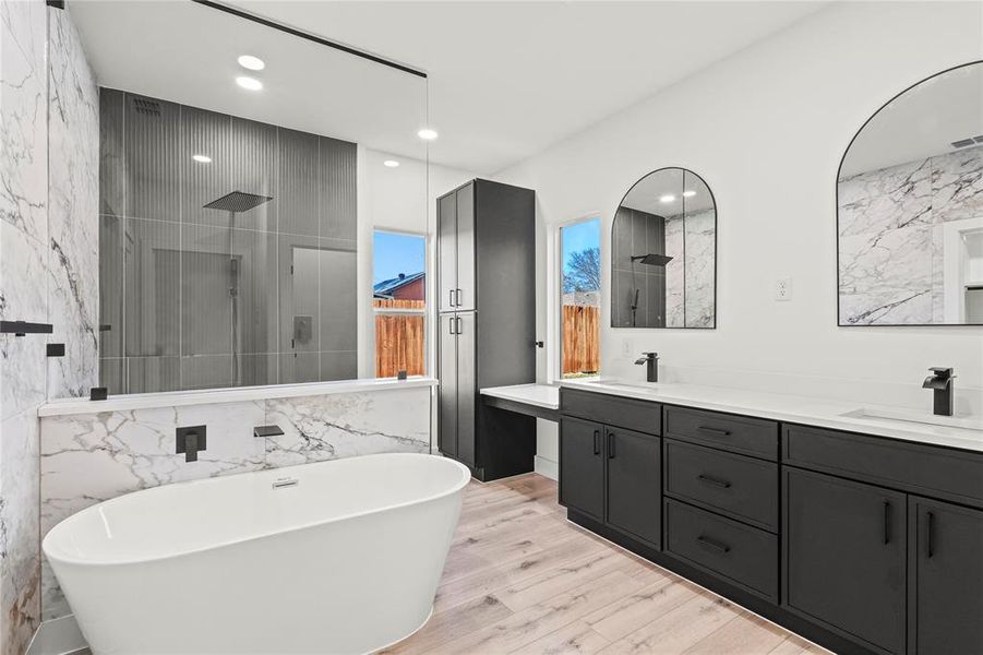 Bathroom with double vanity, a freestanding bath, walk in shower, tile walls, and light wood-style floors