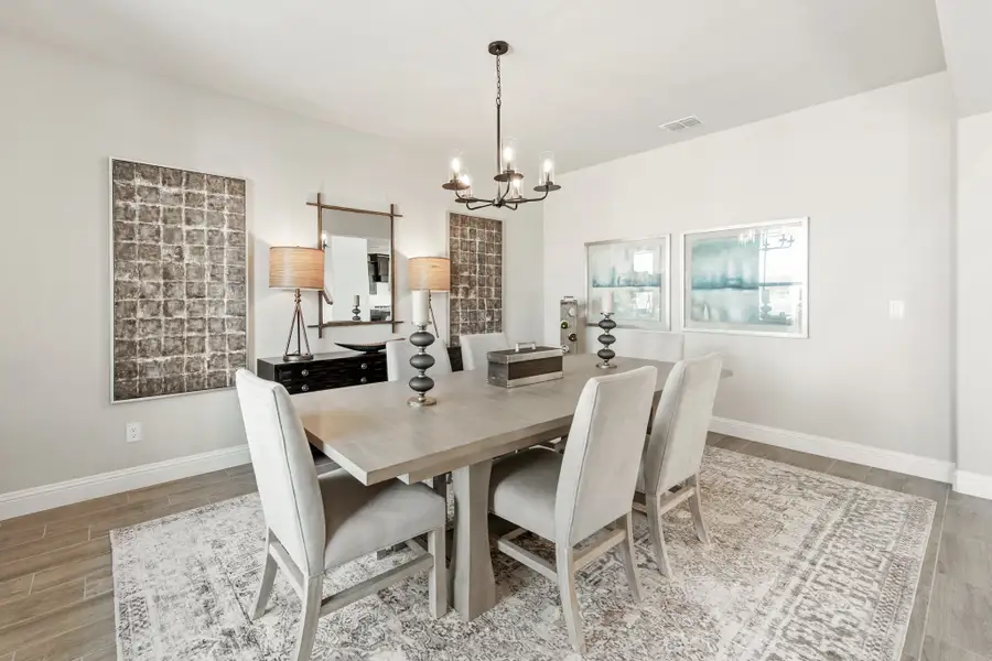 Dining room with gray rectangular table, six upholstered chairs, chandelier, and patterned area rug on hardwood floors Dining room with gray rectangular table, six upholstered chairs, chandelier, and patterned area rug on hardwood floors