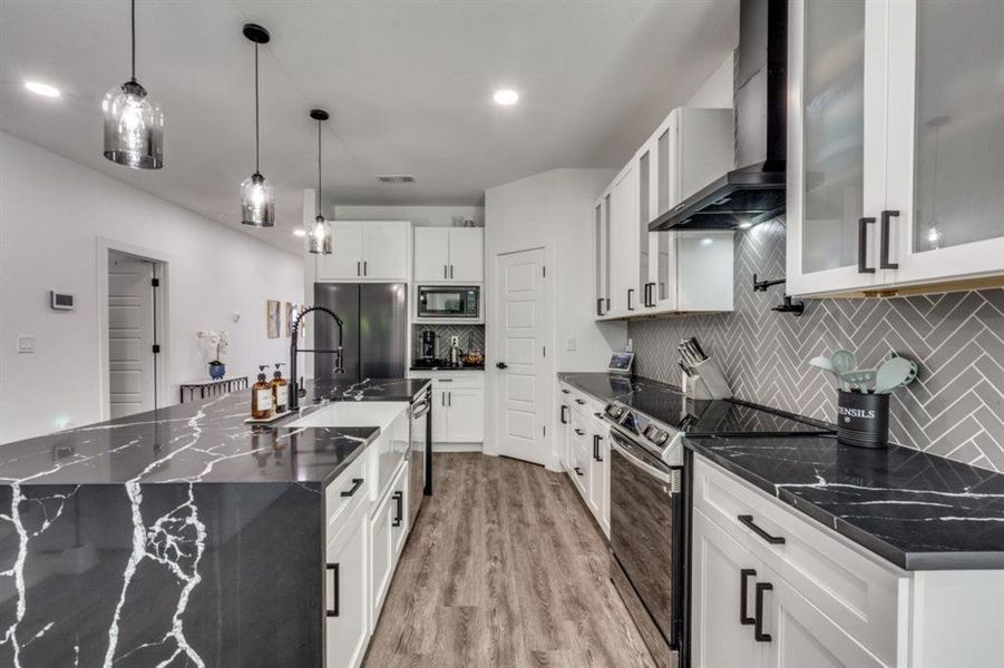 Kitchen with wall chimney range hood, appliances with stainless steel finishes, tasteful backsplash, light wood-type flooring, and white cabinetry