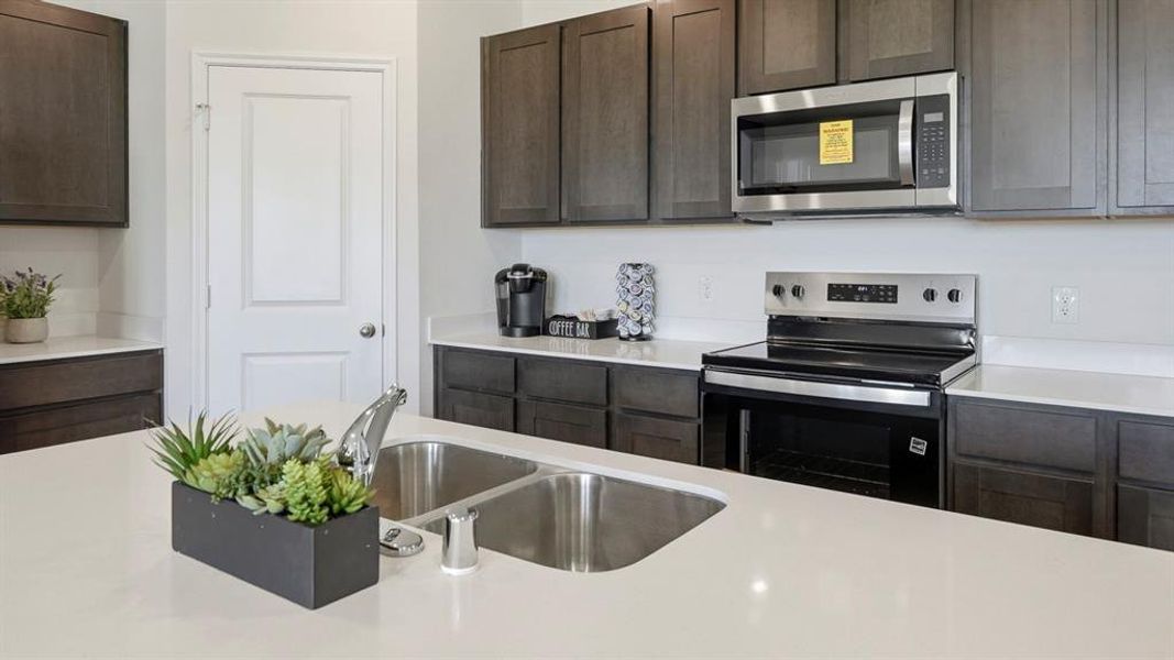 Kitchen featuring stainless steel appliances, dark brown cabinets, and light stone counters Kitchen featuring stainless steel appliances, dark brown cabinets, and light stone counters