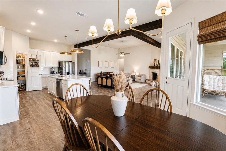 Open-concept dining area featuring wood-finish flooring, a contemporary chandelier, and a white kitchen with a central island