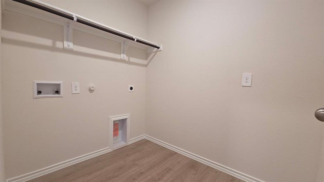 Dedicated utility space featuring light wood-finish flooring, white baseboards, and a wall-mounted clothing rod Dedicated utility space featuring light wood-finish flooring, white baseboards, and a wall-mounted clothing rod
