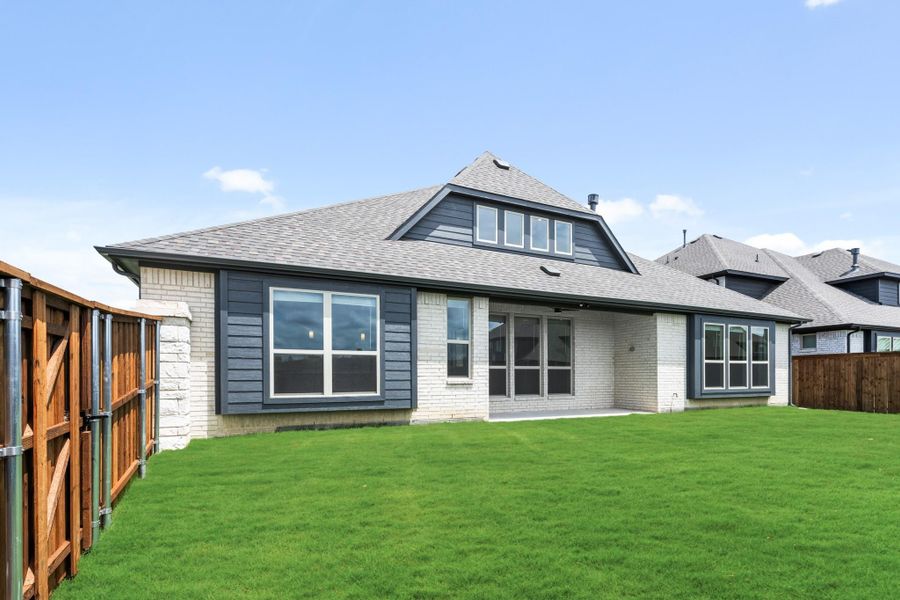 Rear exterior of single-story home with white brick, dark siding, large windows, and fenced backyard with green lawn