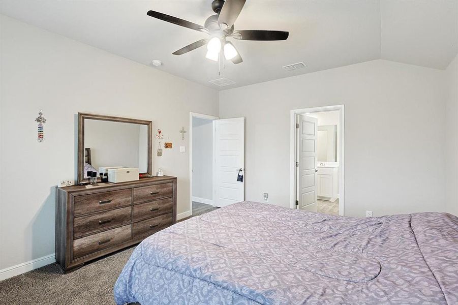 Carpeted bedroom featuring connected bathroom, a ceiling fan, visible vents, vaulted ceiling, and baseboards