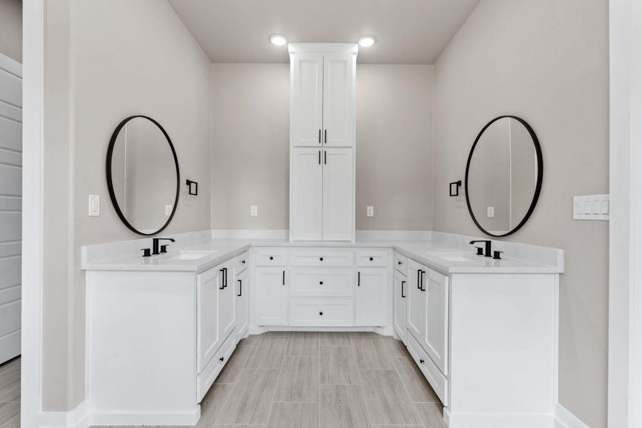 Dual vanities with pristine white countertops and a central storage tower define this bright bathroom. Dual vanities with pristine white countertops and a central storage tower define this bright bathroom.
