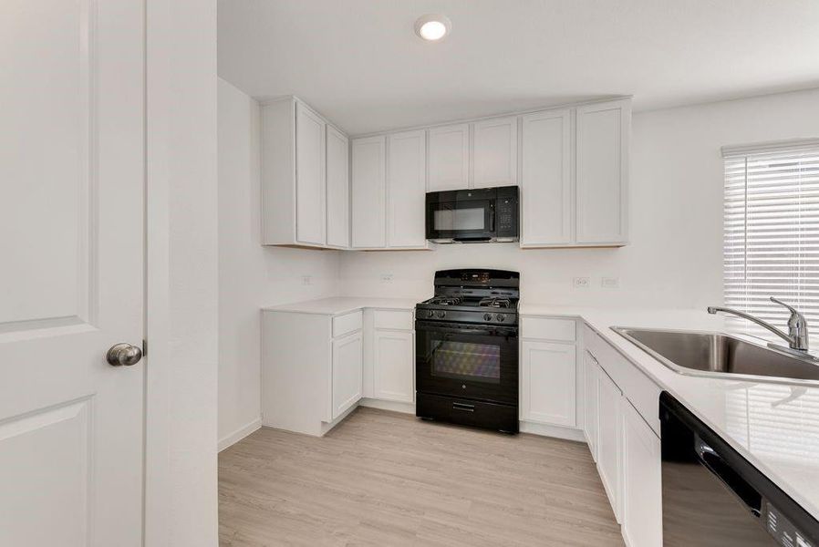 Kitchen with light wood-type flooring, white cabinets, sink, and black appliances