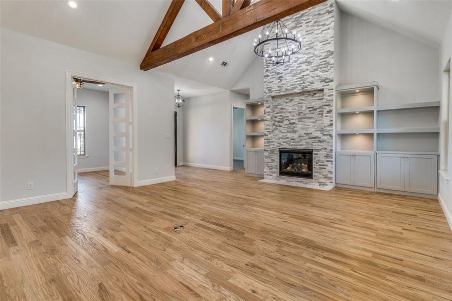 Unfurnished living room with light wood-type flooring, built in shelves, beamed ceiling, a fireplace, and high vaulted ceiling