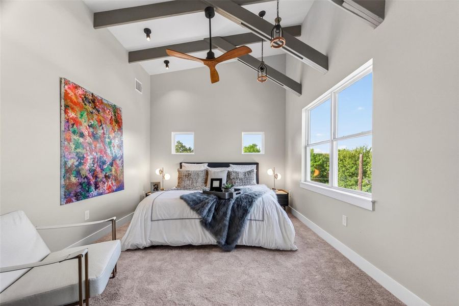 The primary bedroom's gracious proportions capture the full volume of the vaulted beamed ceiling. Natural light pours in from multiple windows and direct access to the primary bath and closet make this a seamlessly functional suite.