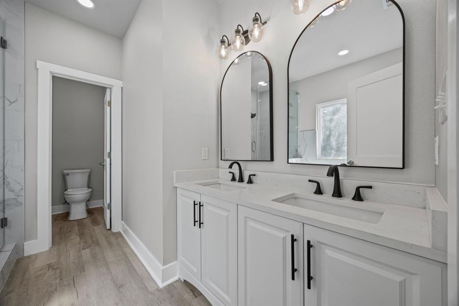 Bathroom featuring double vanity, light wood-style flooring, a marble finish shower, and recessed lighting Bathroom featuring double vanity, light wood-style flooring, a marble finish shower, and recessed lighting