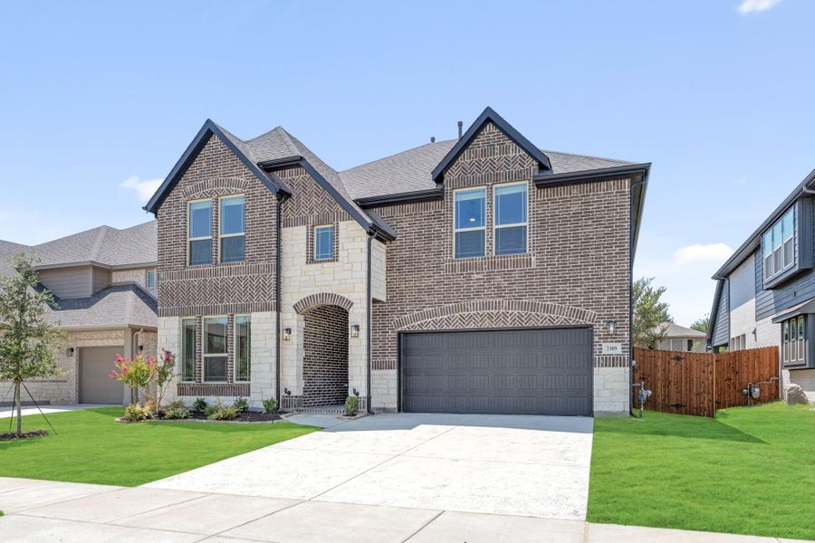 Two-story brick home with stone accents, two-car garage, arched entry, and manicured front lawn