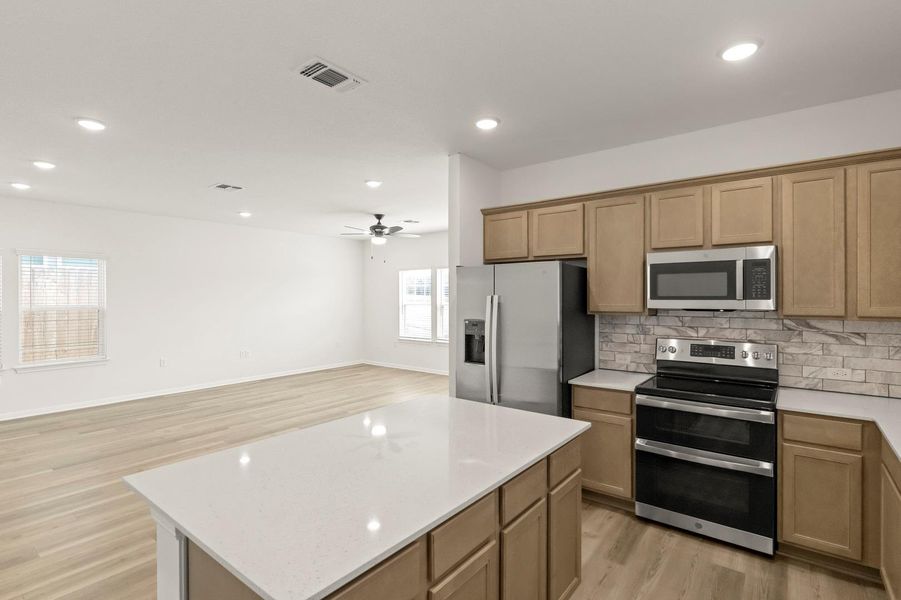 Kitchen with stainless steel appliances, a kitchen island, open floor plan, light wood-type flooring, and recessed lighting