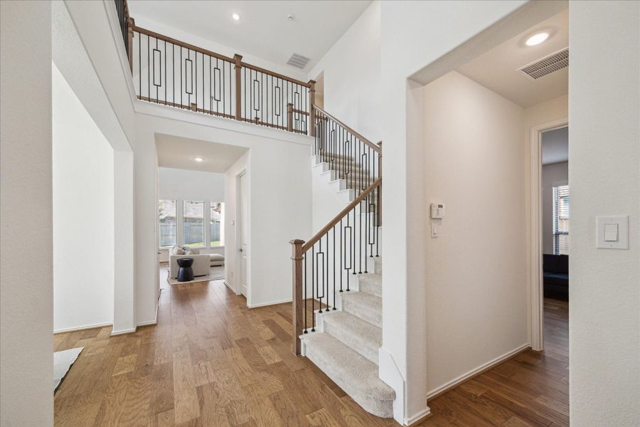 From the foyer, a long hall leads into the main living area, where engineered hardwood flows seamlessly throughout the first floor. An elegant staircase and soaring ceilings create an open, airy ambiance that elevates the home’s design.