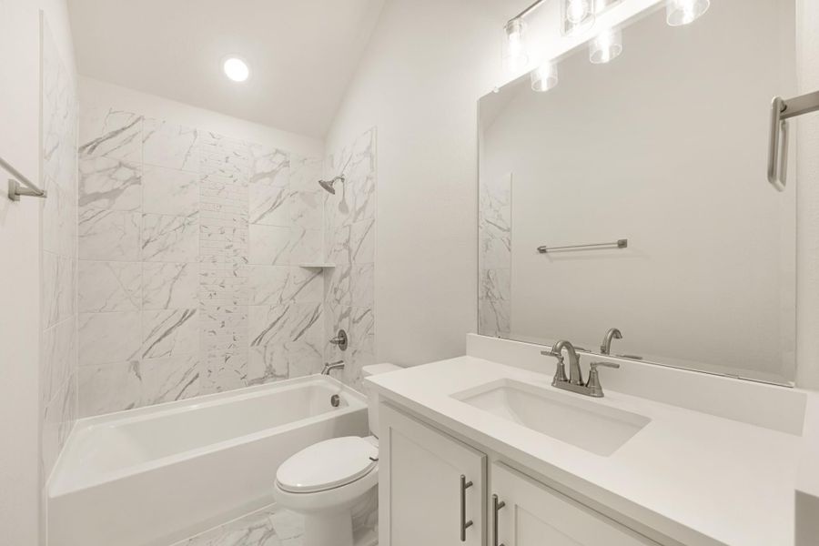 Bathroom with marble-tile tub surround, white vanity with quartz countertop, and vaulted ceiling