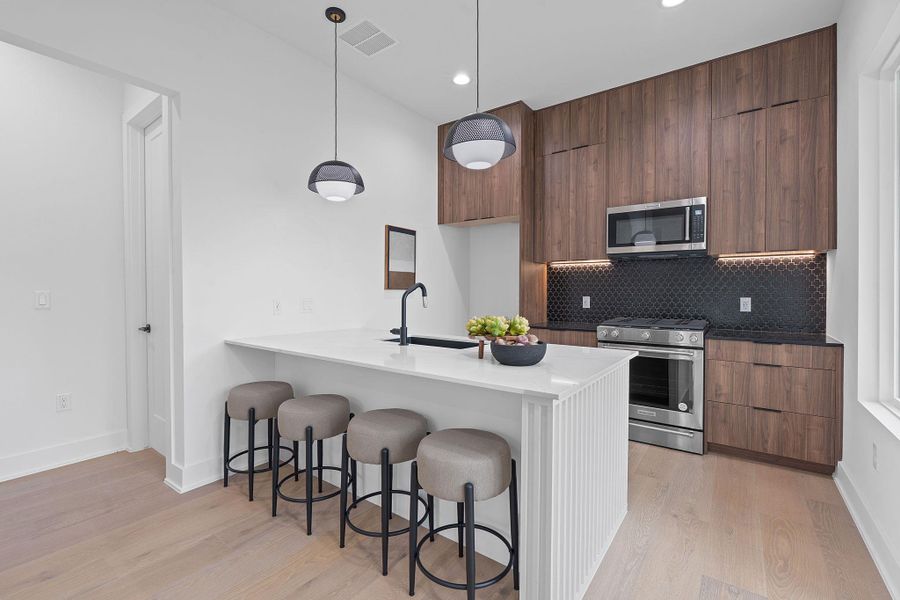 Kitchen with stainless steel appliances, modern cabinets, a breakfast bar area, light wood finished floors, and recessed lighting