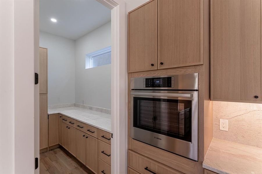 Kitchen with stainless steel oven, decorative backsplash, light stone countertops, light wood-type flooring, and light brown cabinetry