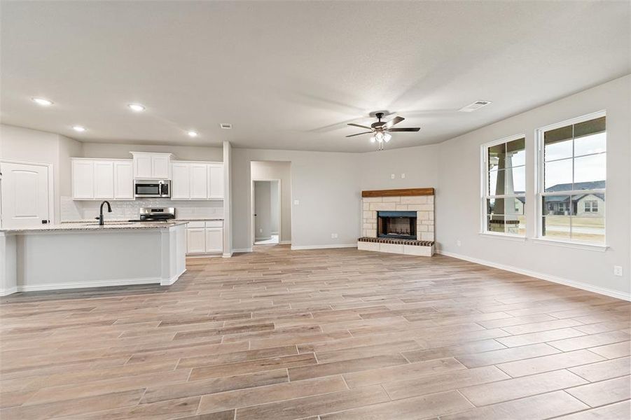 Unfurnished living room with a ceiling fan, wood finish floors, recessed lighting, and a stone fireplace Unfurnished living room with a ceiling fan, wood finish floors, recessed lighting, and a stone fireplace