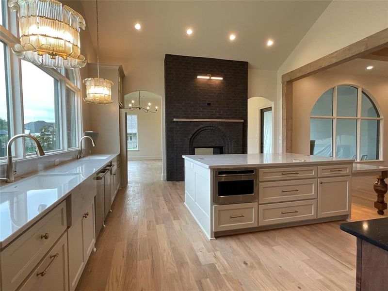 Kitchen with a sink, a fireplace, a chandelier, white cabinetry, and light wood-type flooring