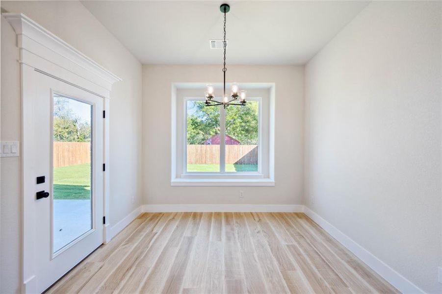 Unfurnished dining area featuring a chandelier, a wealth of natural light, and light hardwood / wood-style flooring