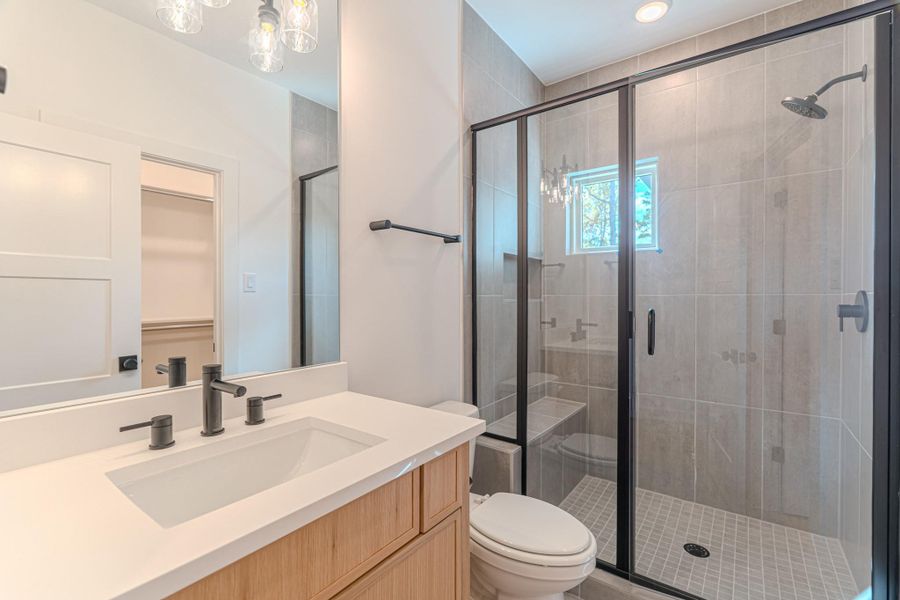 This bathroom features a modern design with a sleek glass-enclosed shower, large vanity with black fixtures, and bright lighting.