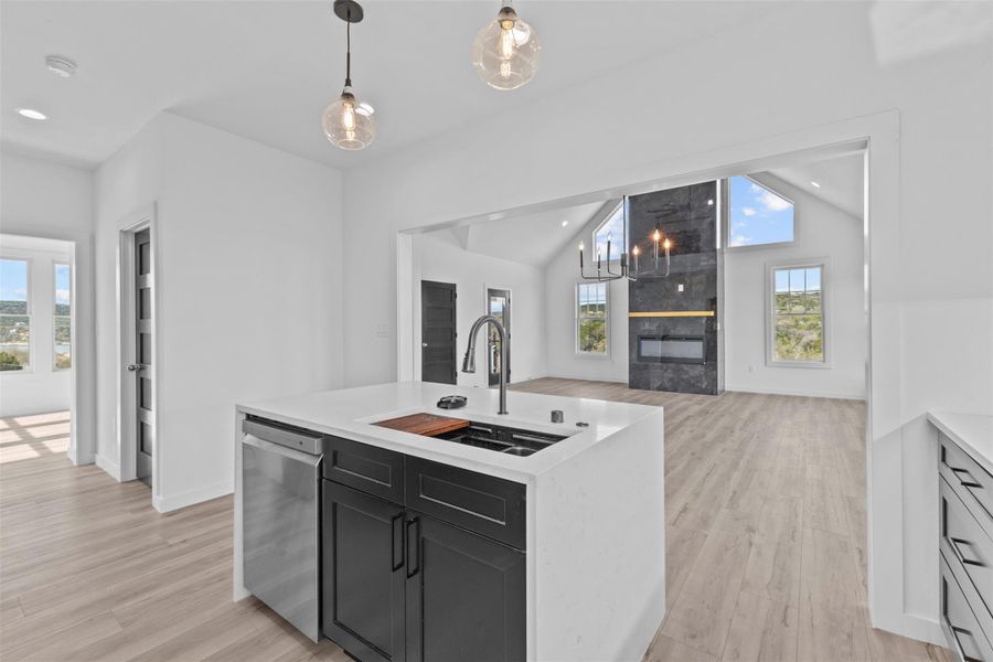 Kitchen with an island with sink, open floor plan, stainless steel dishwasher, pendant lighting, and light wood-style floors