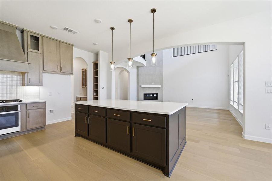 Expansive kitchen island with dark wood-finish cabinetry, a light-toned countertop, and three pendant lights Expansive kitchen island with dark wood-finish cabinetry, a light-toned countertop, and three pendant lights