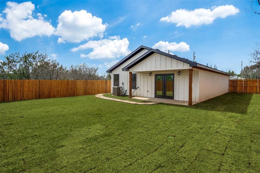 Rear view of property featuring a lawn, french doors, central AC, and a fenced backyard