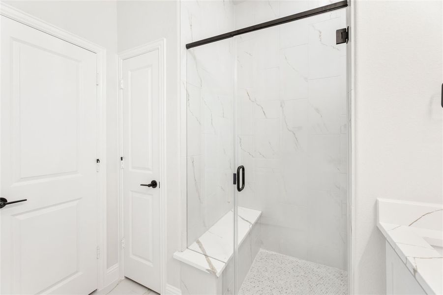 Walk-in shower with marble tile walls, built-in bench, glass door, and black hardware accents