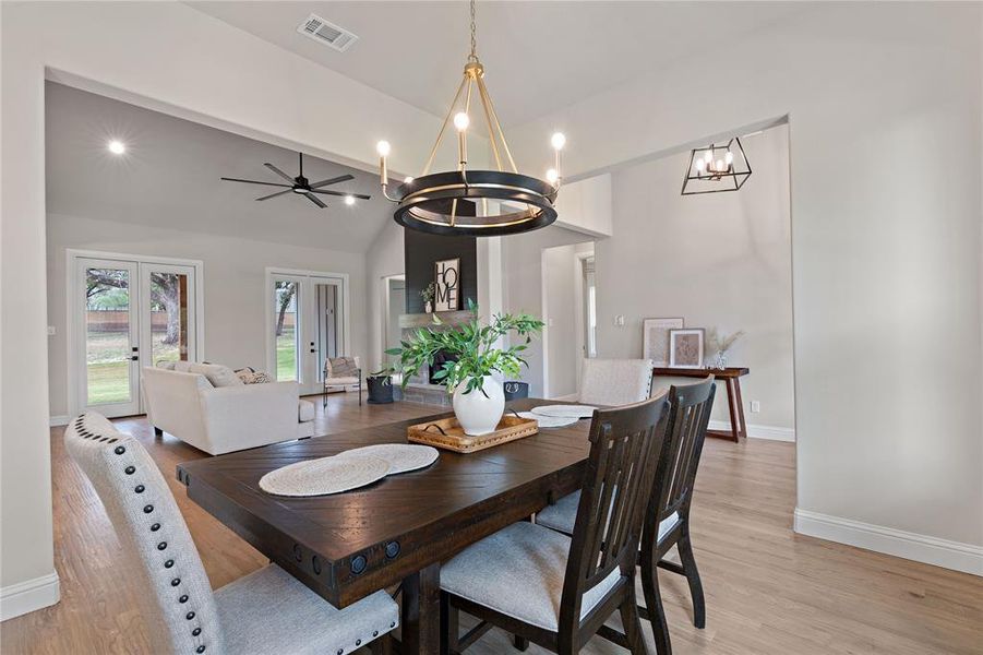 Dining area featuring vaulted ceiling with beams, french doors, ceiling fan with notable chandelier, and light wood-type flooring