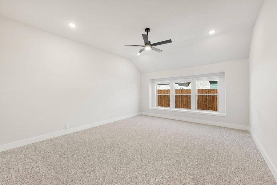 Empty bedroom with vaulted ceiling, ceiling fan, carpet flooring, and large window