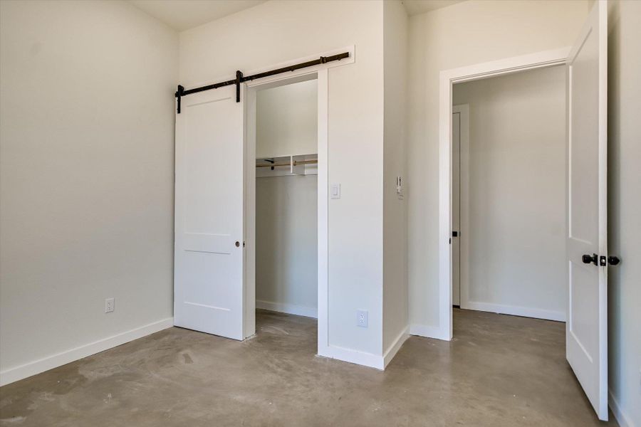 Unfurnished bedroom with concrete flooring, a barn door, and a closet