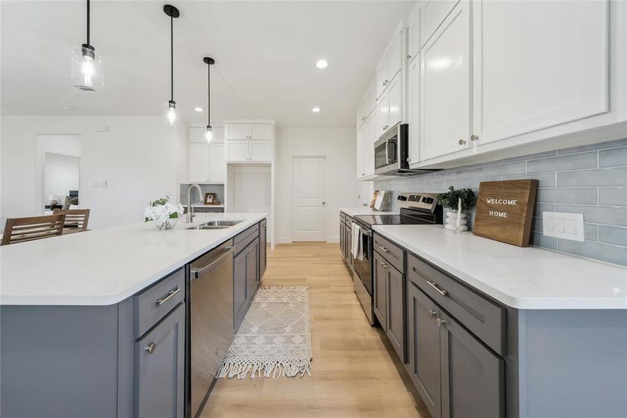 Kitchen featuring sink, white cabinetry, hanging light fixtures, a center island with sink, and stainless steel appliances