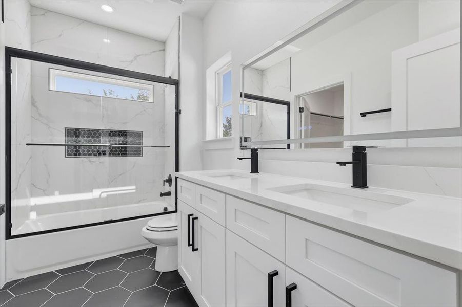 Full bathroom with shower / bath combination with glass door, double vanity, and dark tile patterned flooring Full bathroom with shower / bath combination with glass door, double vanity, and dark tile patterned flooring