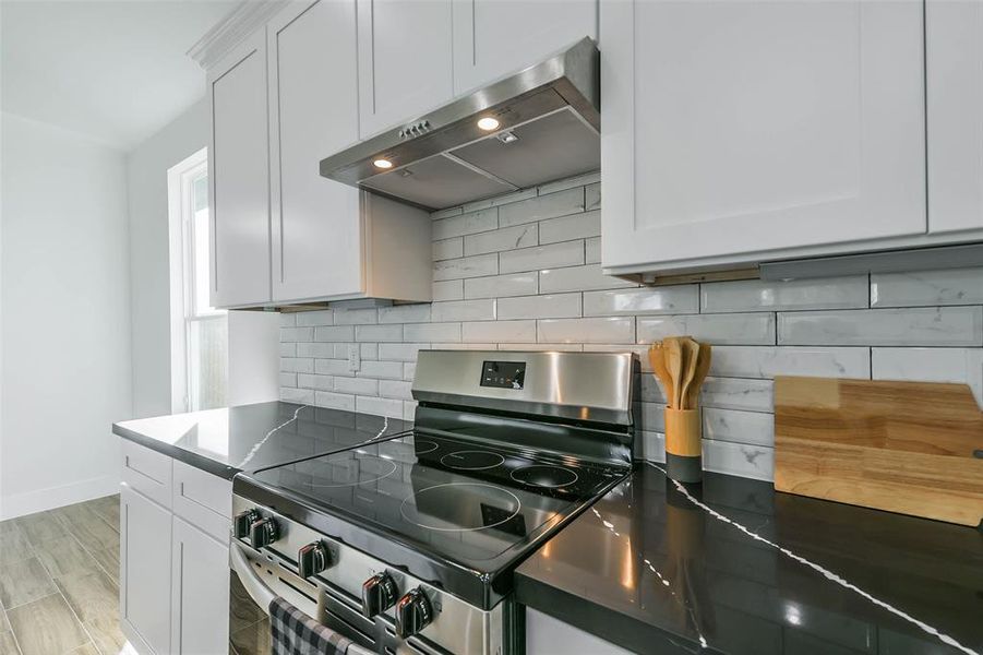 This modern kitchen features sleek white cabinetry, glossy black countertops, and a classic subway tile backsplash, complemented by stainless steel appliances and light wood flooring.