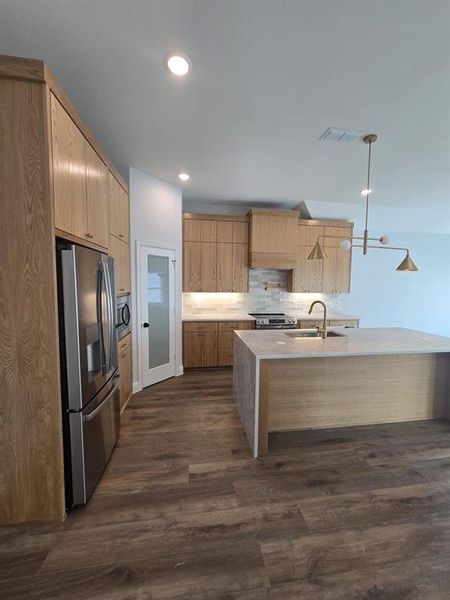 Kitchen featuring light stone countertops, appliances with stainless steel finishes, dark wood-style floors, backsplash, and decorative light fixtures