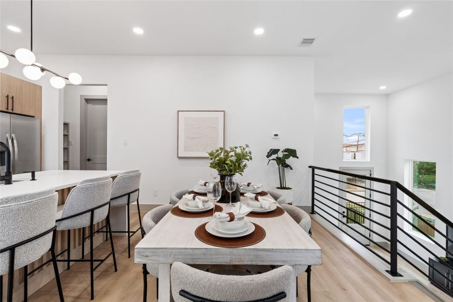 Perched above the split-level living room, this open-concept kitchen and dining area strikes a perfect balance of function and flow. Sleek lighting, modern finishes, and an airy sightline over the railing create a sense of connectivity, while natural light pours in from double-height windows just beyond. Ideal for both entertaining and everyday living.