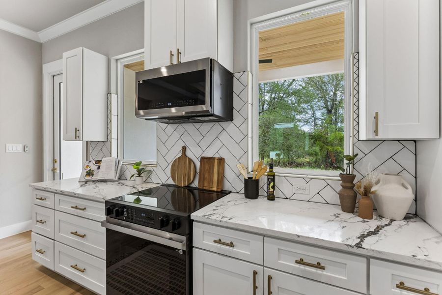 A contemporary kitchen features bright white cabinetry, elegant marble-patterned countertops, and a chic herringbone tile backsplash.