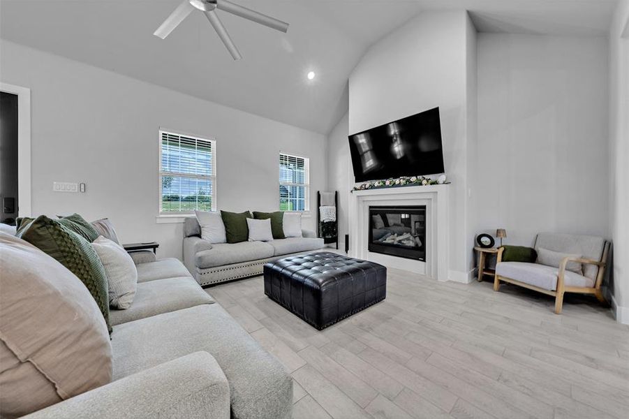 Vaulted ceiling living area featuring a built-in fireplace with white mantel, light wood-finish flooring, and multiple windows