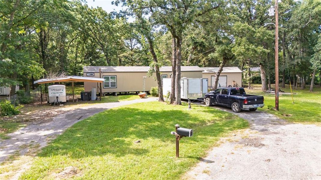 Manufactured / mobile home featuring a front lawn, asphalt driveway, and view of wooded area
