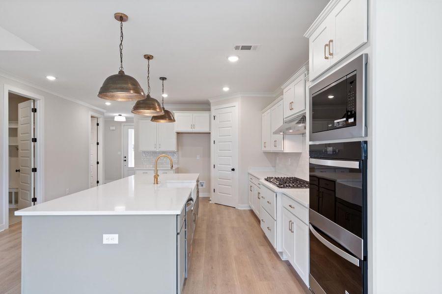 Spacious kitchen featuring an island with a brass-finish faucet, built-in stainless steel appliances, white cabinetry, and wood-finish flooring Spacious kitchen featuring an island with a brass-finish faucet, built-in stainless steel appliances, white cabinetry, and wood-finish flooring