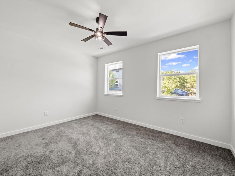 Bright interior space featuring a ceiling fan with integrated lighting, two windows with white trim, gray carpet flooring, and clean white walls