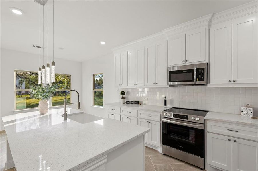 Kitchen with appliances with stainless steel finishes, white cabinets, a center island with sink, and pendant lighting