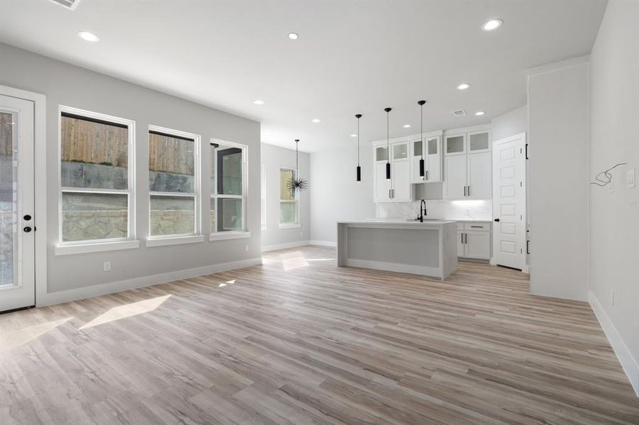 Kitchen featuring pendant lighting, white cabinetry, tasteful backsplash, light hardwood / wood-style floors, and an island with sink